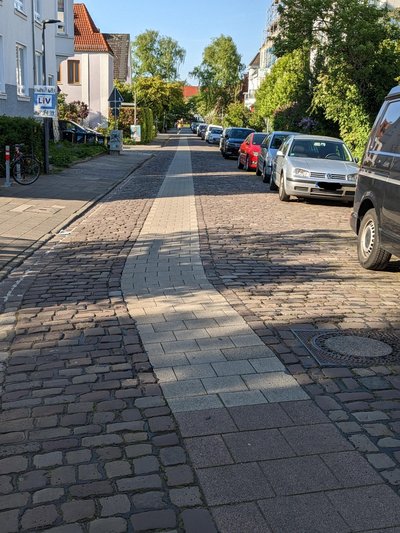 Kopfsteinpflasterstraße mit glattem Pflasterstreifen in der Mitte.